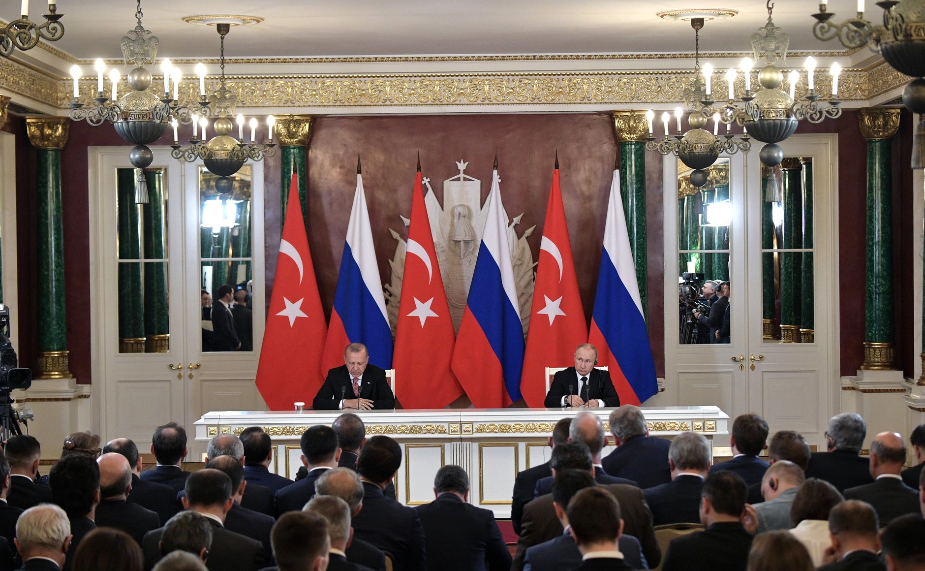 President Putin and President Erdogan sit at a table in front of the Turkish and Russian flags, in front of a room full of reporters.
