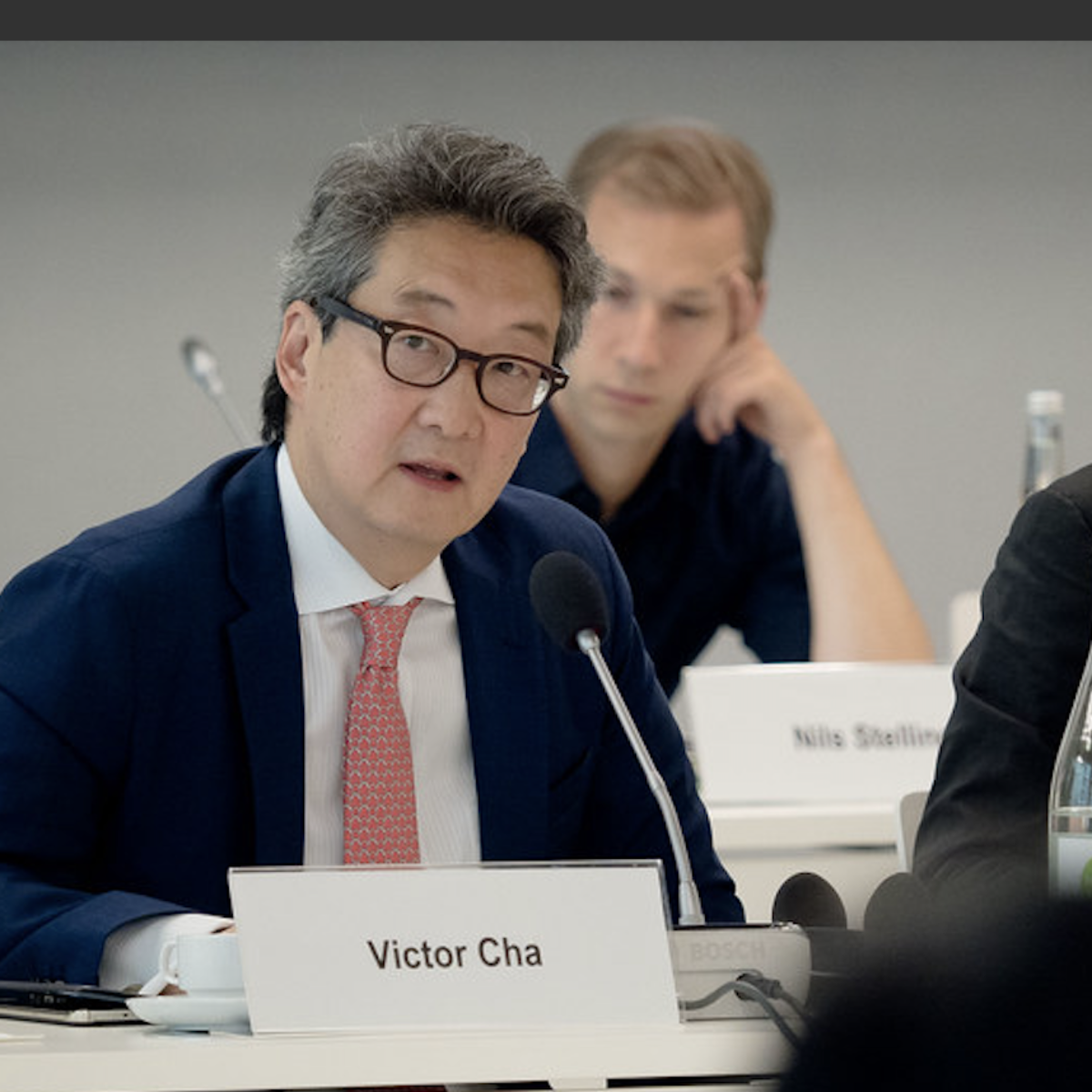 A man sits at a table behind a placard that reads 