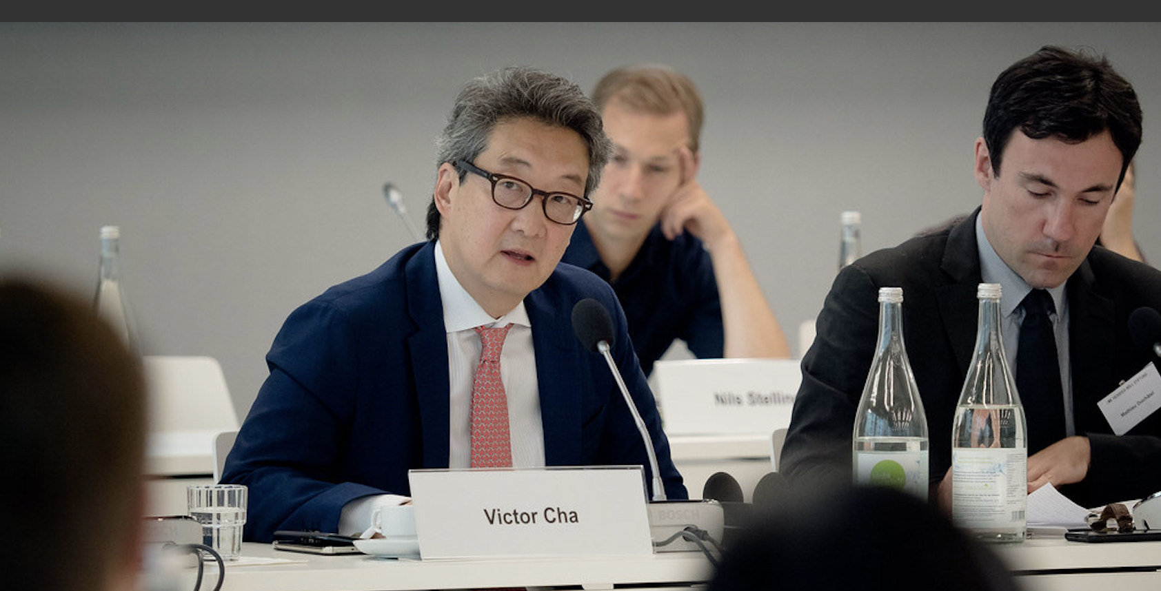 A man sits at a table behind a placard that reads 