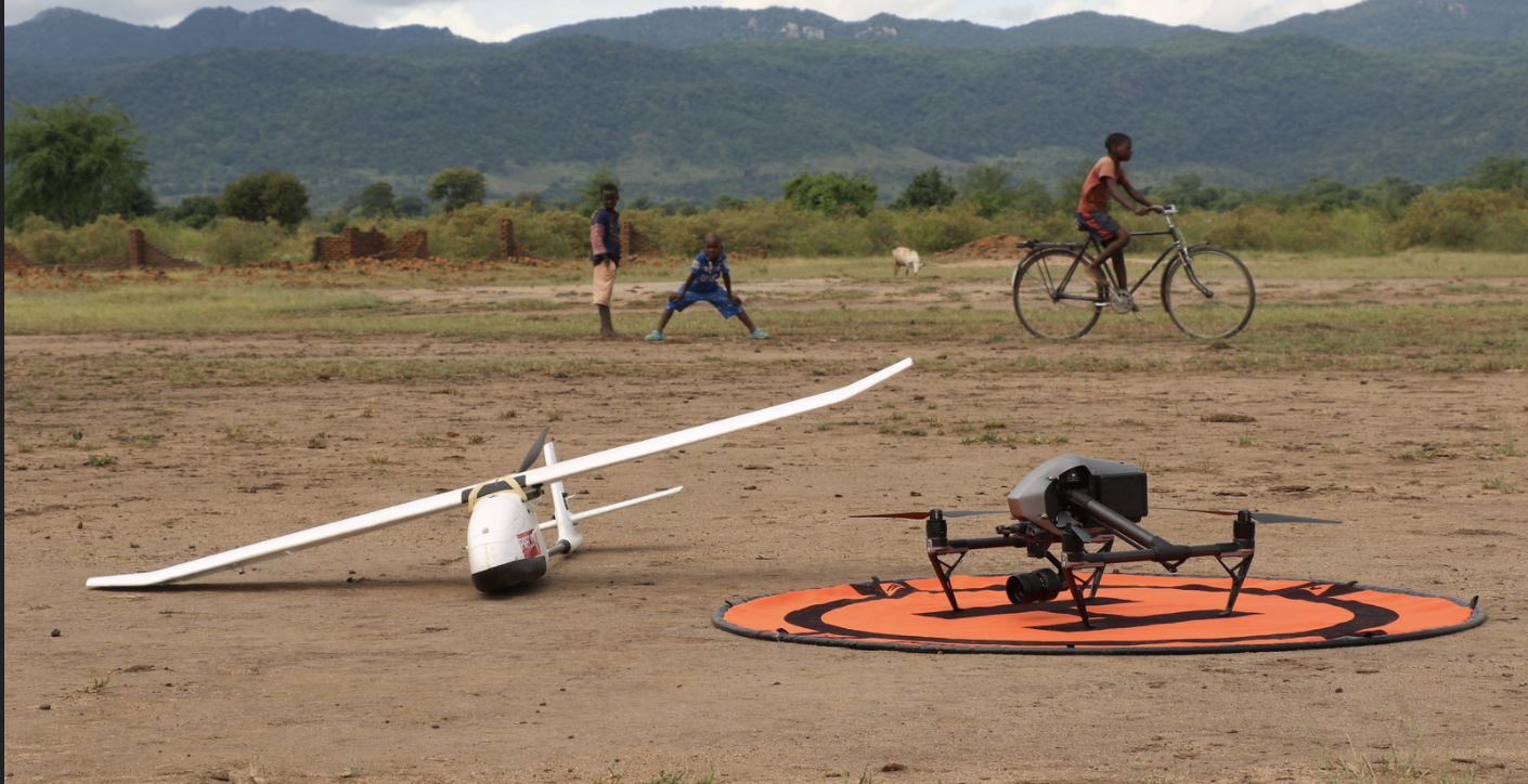 Two small drones sit rest on the dirt against the backdrop of mountains.