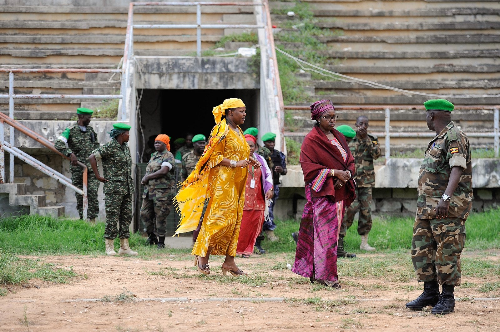 Three women in brightly colored clothing walk among soldiers in camouflage.