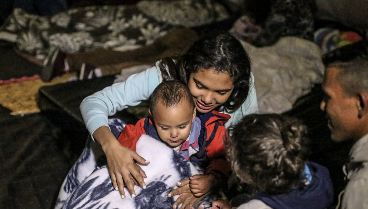 A Venezuelan mother and two of her children sit playing in a temporary shelter tent for migrants.