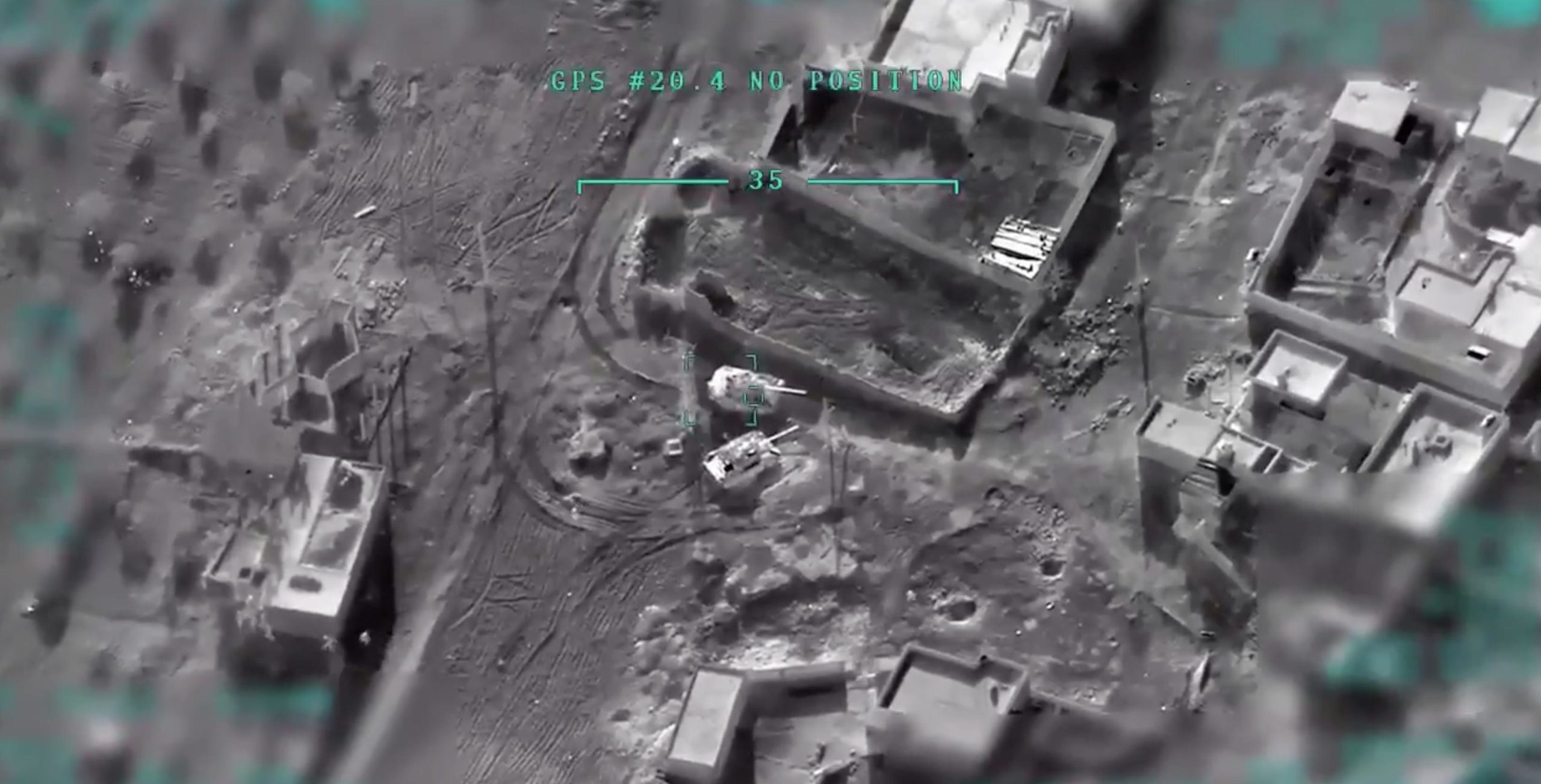 A gray image taken from Turkish drone footage showing buildings, terrain, and tanks from overhead.