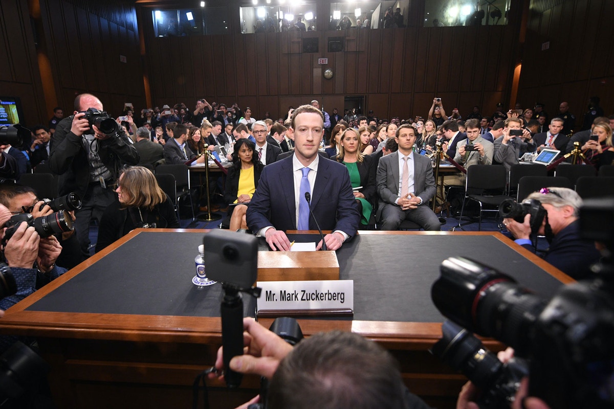 A man sits in front of an audience and cameras