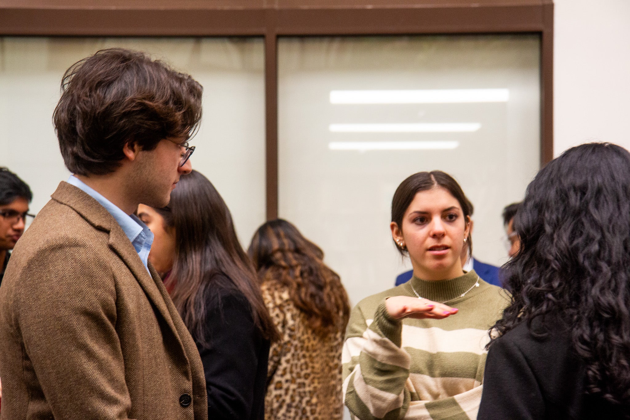 A group of students engages in a discussion. One student gestures while speaking, and others listen attentively in a casual setting.