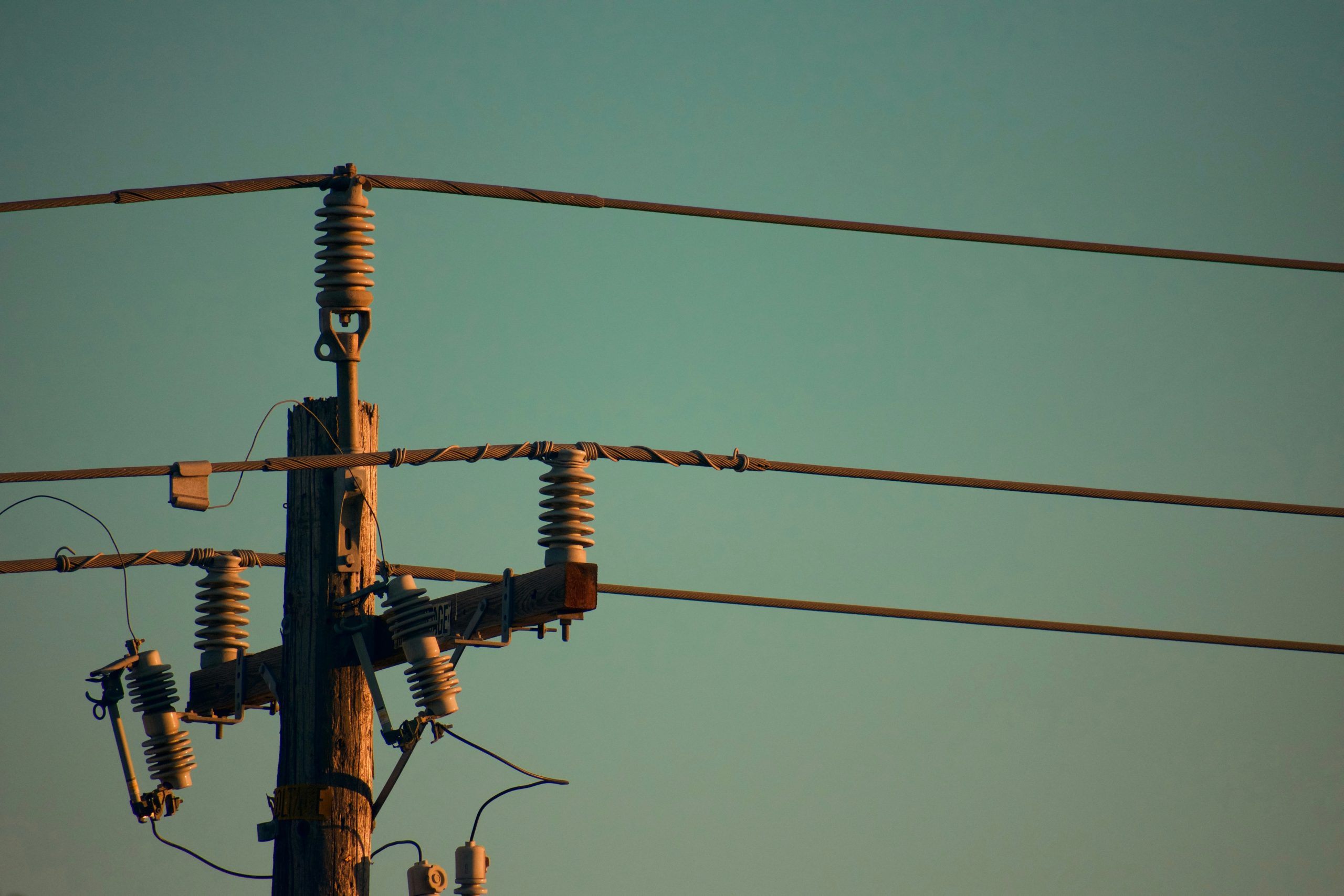 Close-up of an electricity utility pole at dusk, showing detailed components like insulators and electrical wires against a clear sky.